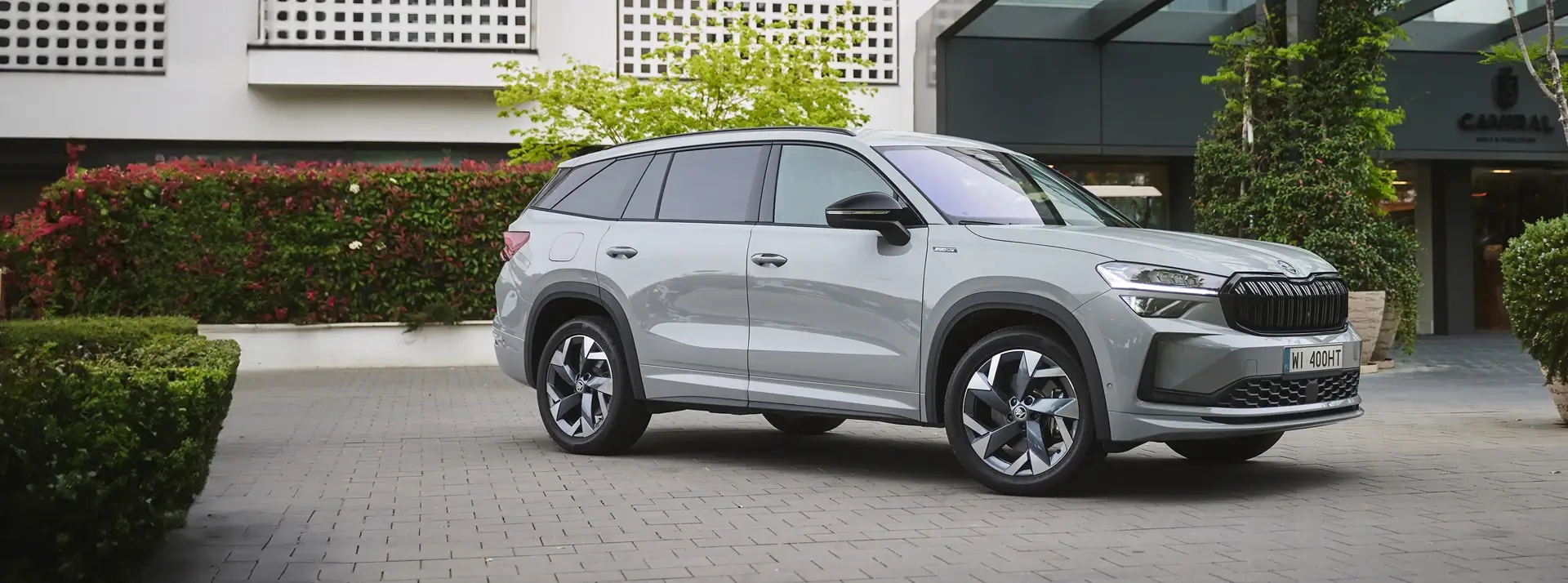 parking przed nowoczesnym hotelem, krzewy, donice z drzewami i szara Skoda Kodiaq