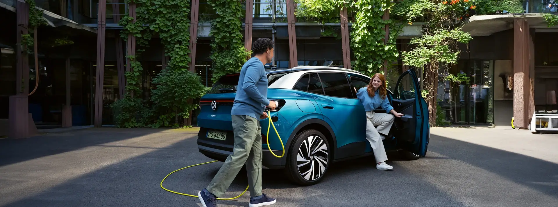 samochód elektryczny Volkswagen ID.5, mężczyzna podłącza go do ładowania, kobieta wysiada z auta